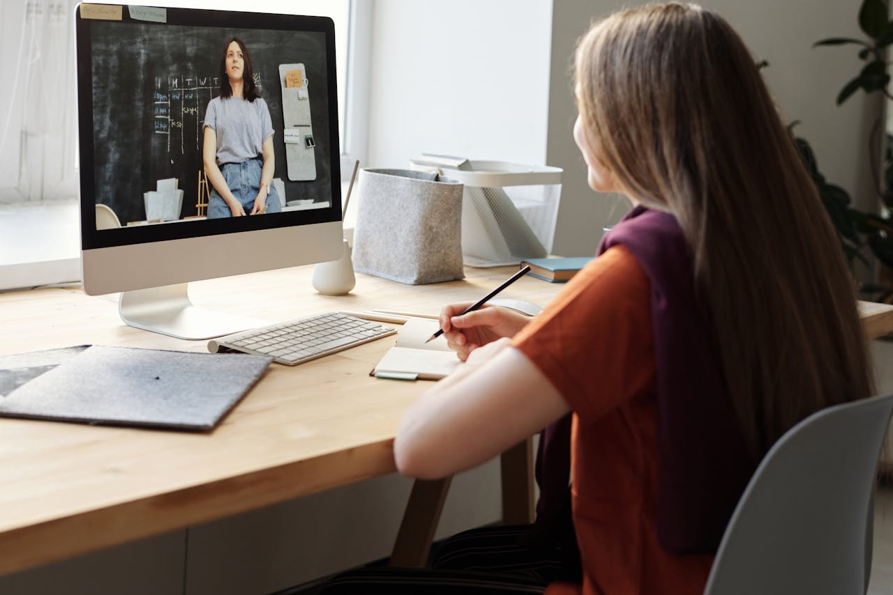 about-us Teen girl attending an online class at home, takes notes at her desk.