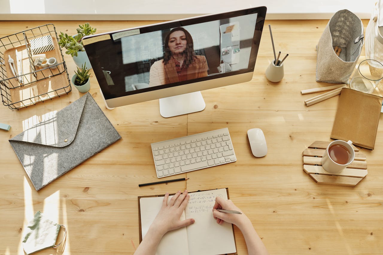 who-we-are Person taking notes during a video call at a neatly organized home desk, showing remote work lifestyle.